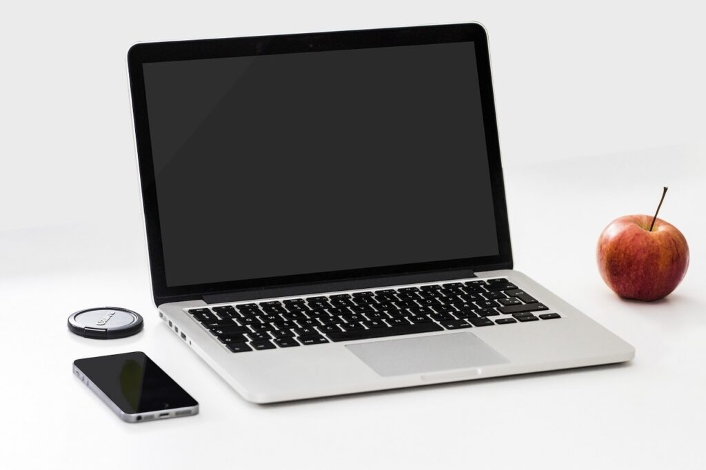 This image shows that the laptop with a smartphone and apple in the table.