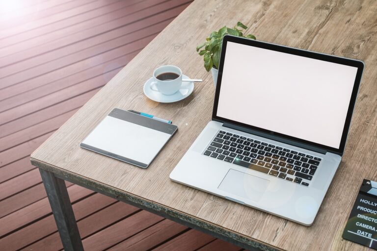 This image shows the Apple MacBook Pro 2022 with a cup of coffee and notebook in the table.